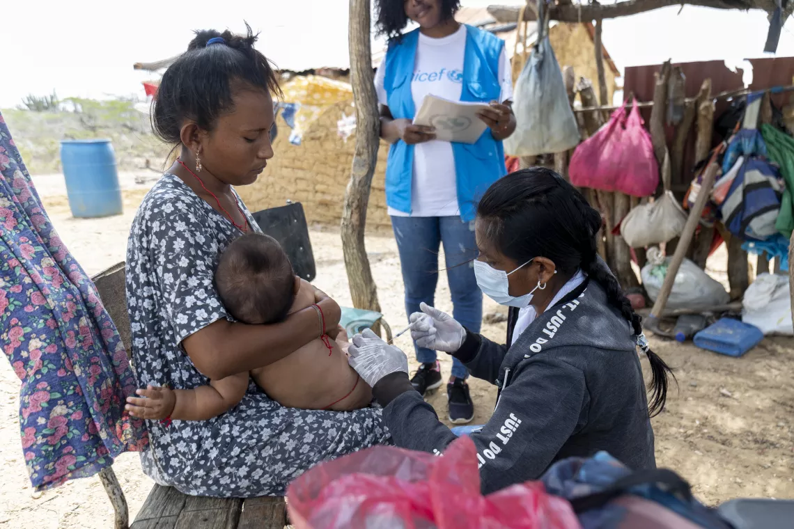 Colaborador de uNICEF vacunando a un niño que esta en brazos de su madre