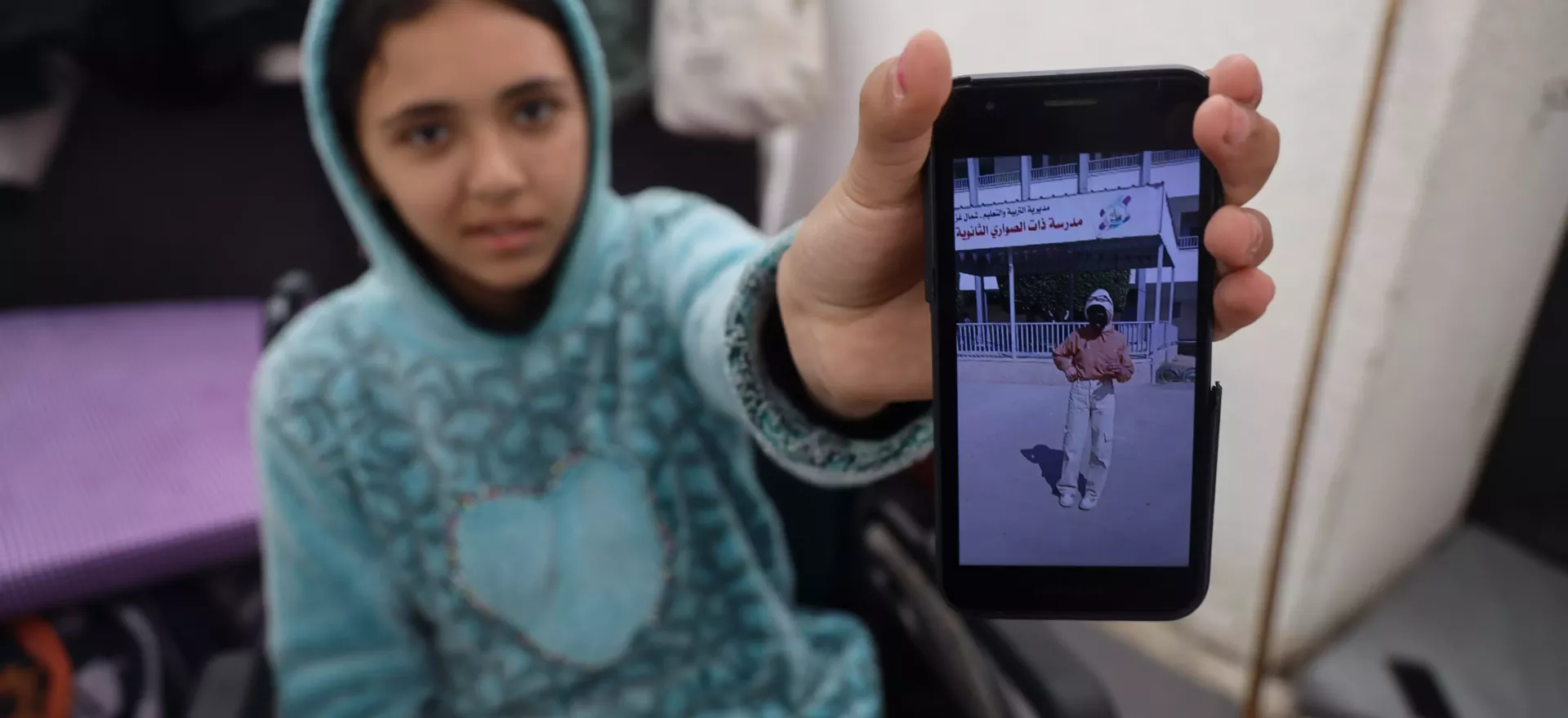 Una niña sentada en silla de ruedas sostiene su teléfono móvil para mostrar una foto de sí misma antes de sufrir una lesión.