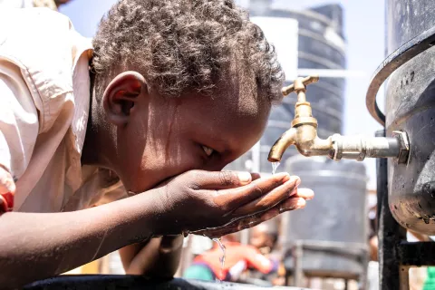 Un enfant utilise ses mains pour boire de l'eau à un robinet