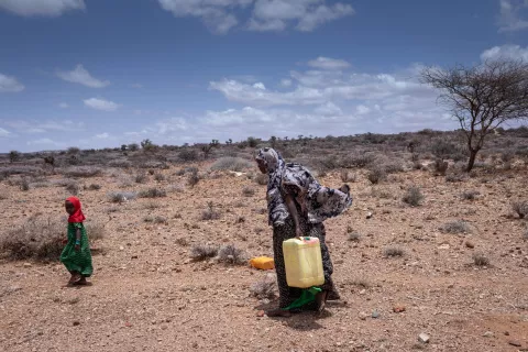 Une femme et une jeune fille transportent des bidons d'eau dans le désert. 