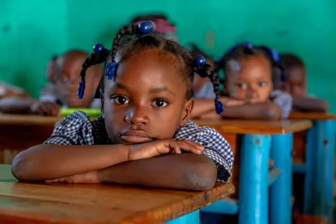 Haiti. Une petite fille est assise à un bureau d'école les bras croisés.