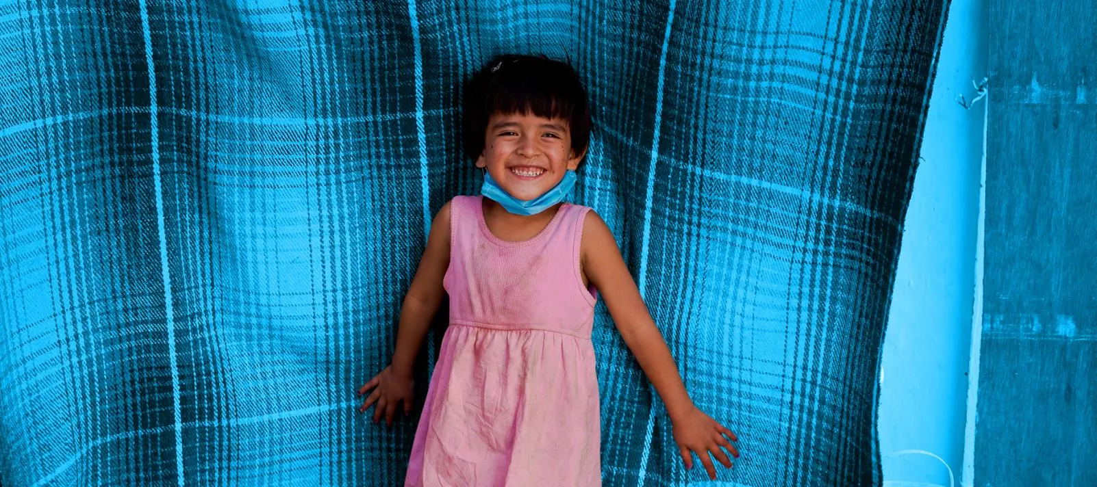 Une petite fille sourit. Elle porte une robe rose
