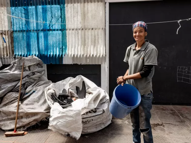 A woman holds a plastic bucket outside a waste drop-off point.