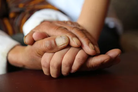 A close up shot of Naku, 85, holding the hands of his grandson, Kelzang Yeshi, 7.