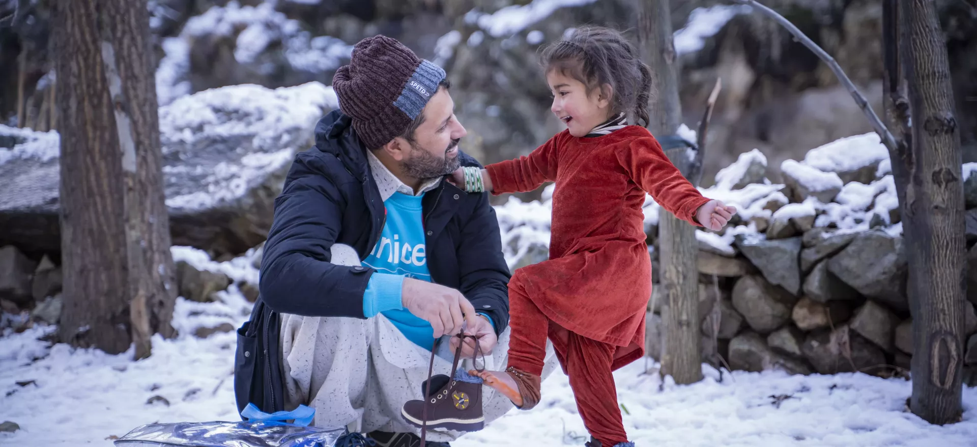 Un enfant met des chaussures neuves avec l’aide d’un agent de l’UNICEF. Dans un paysage enneigé. 