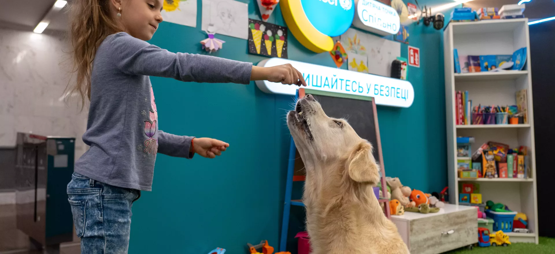 A girl feeds a treat to a dog in a classroom.