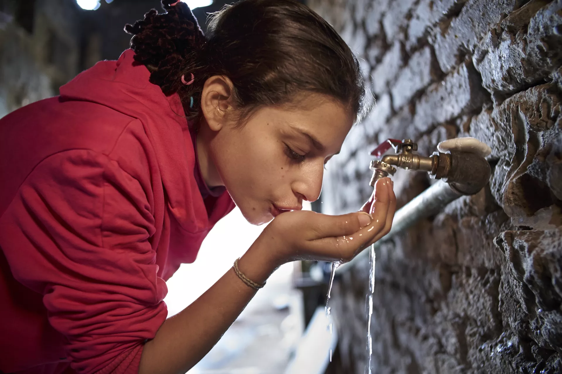 Une jeune fille boit de l’eau à un robinet. 