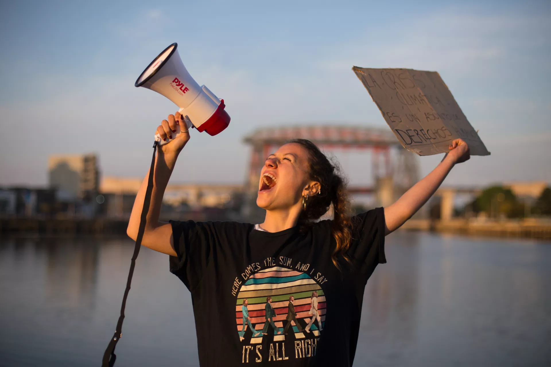 A nineteen-year-old climate activist in Argentina stands outside, arms in air, shouting into a bullhorn.