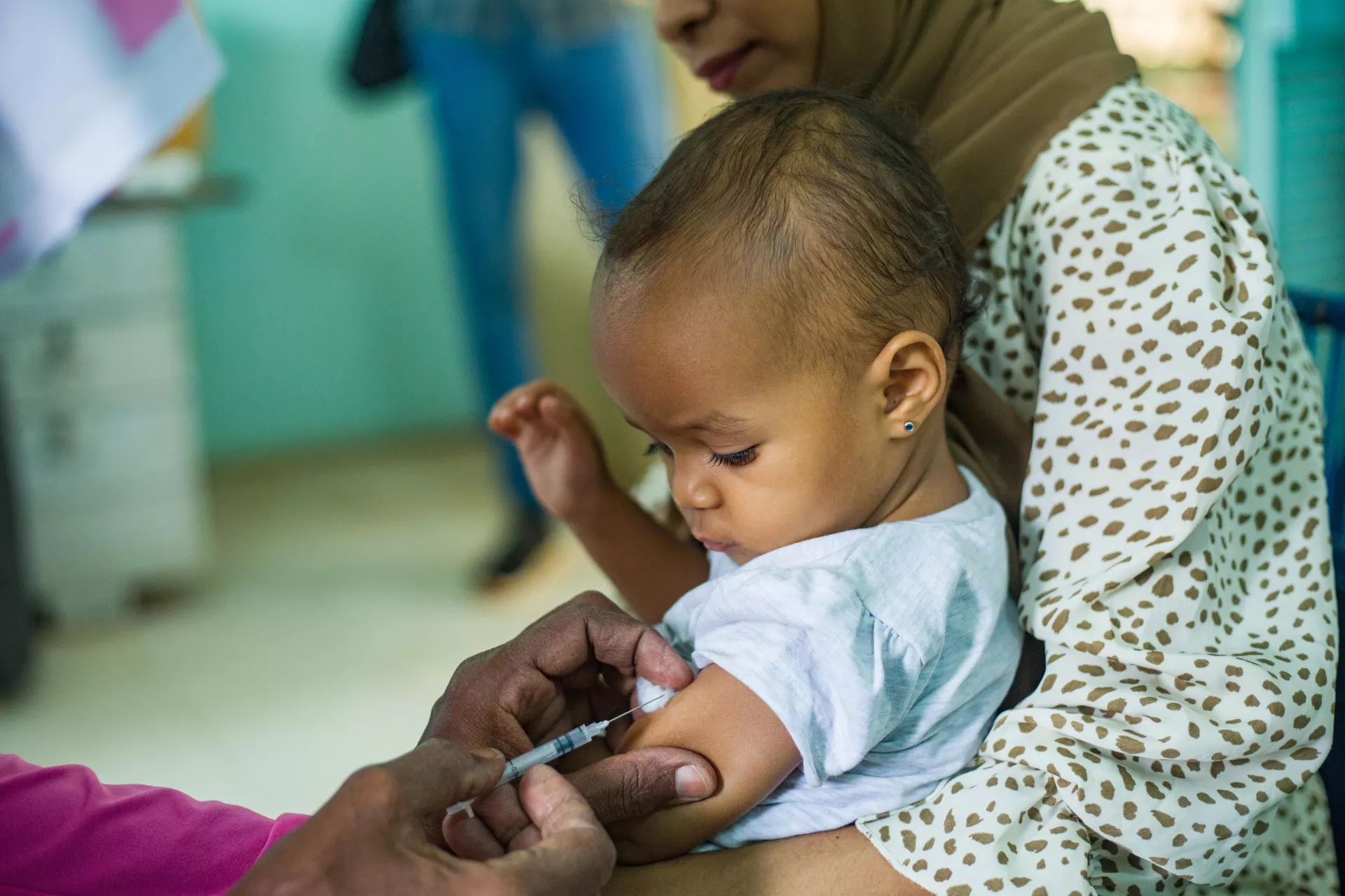 一个小男孩坐在妈妈的腿上，低头看着自己即将接种疫苗的手臂