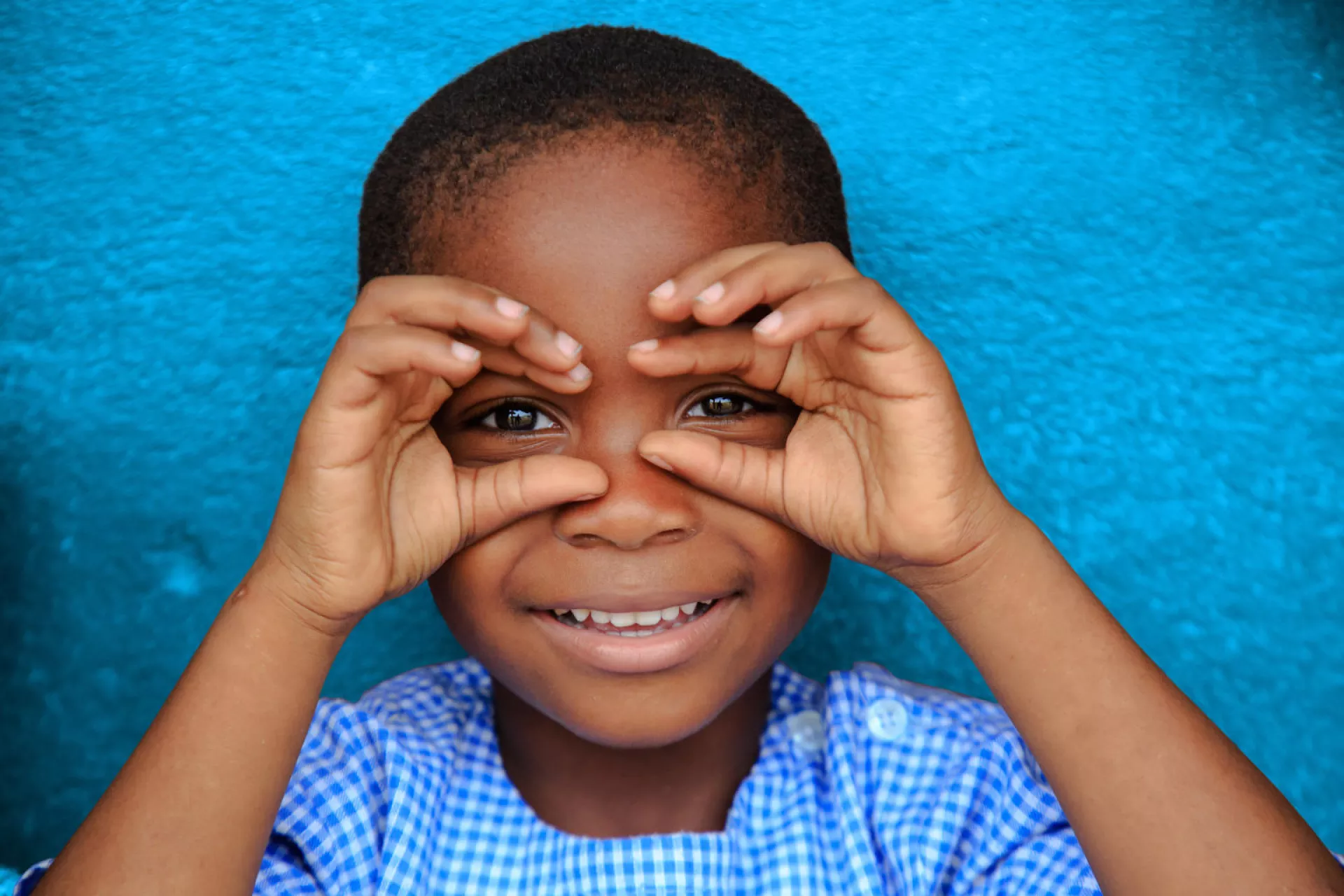 A young boy dressed in blue smiles outside a preschool in Côte d'Ivoire, in 2019.