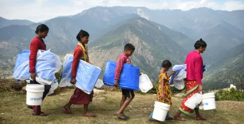 Children and families in Nepal walk carrying supplies