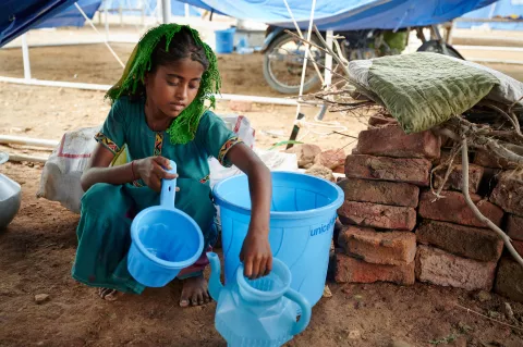 Une fille collecte de l'eau dans un bidon bleu 