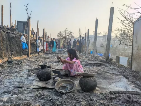 A child stands among rubble of shelters after fire.