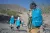 Vue de dos. Des enfants portant un sac à dos UNICEF marchent sur une route de montagnes.