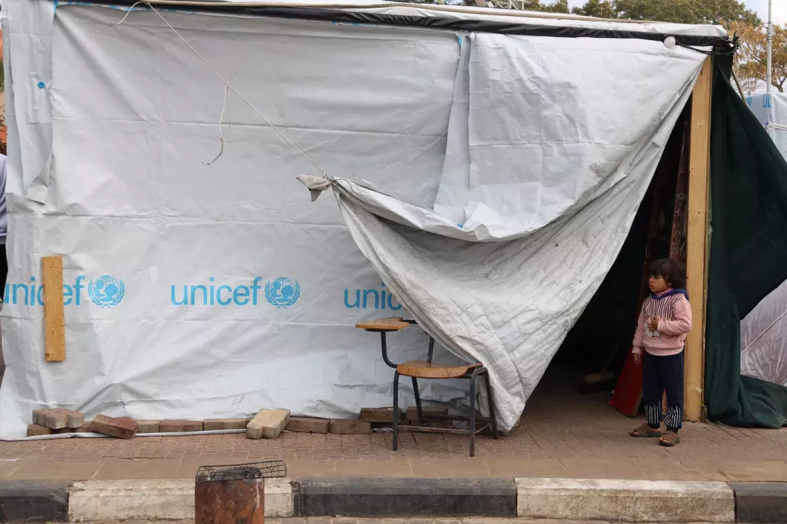 State of Palestine. a small child stands next to a UNICEF tent at a shelter centre in the Gaza Strip.