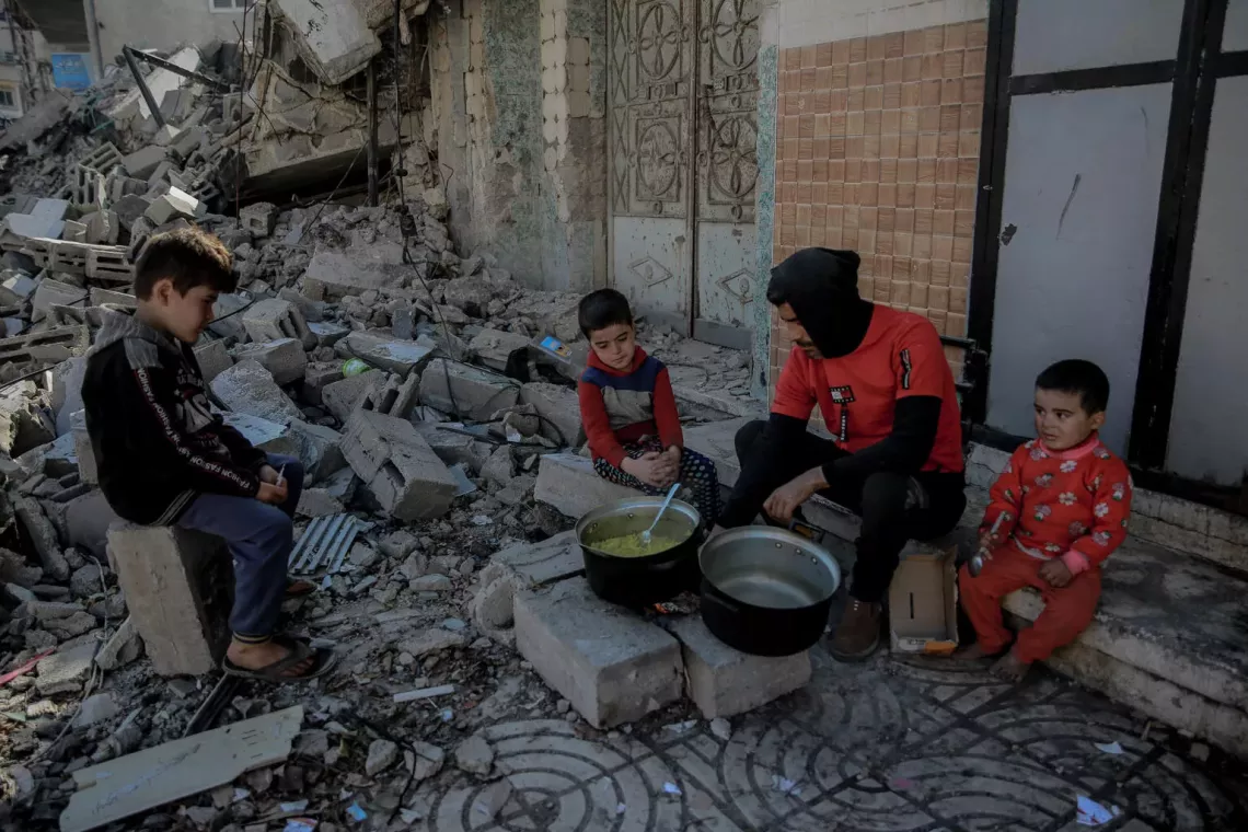 Bande de Gaza. Une famille prépare un repas à l'extérieur, près de piles de décombres provenant de bâtiments détruits.