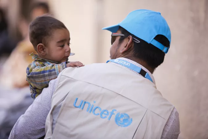  أخصائي حماية الأطفال في اليونيسف في سوريا يحمل طفلاً.