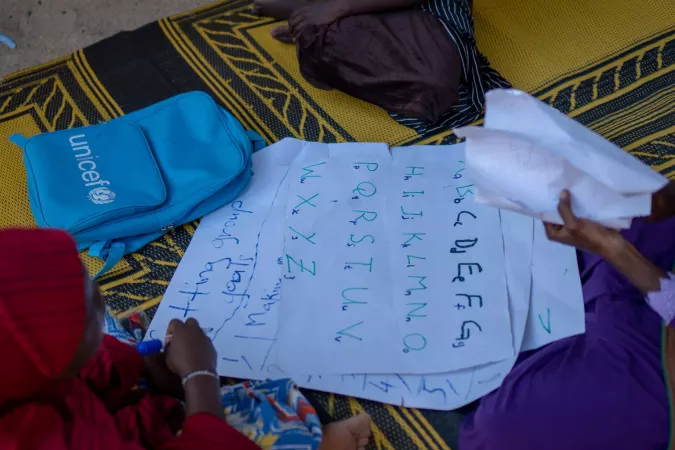 A UNICEF backpack and papers with alphabet written on it are on the floor.