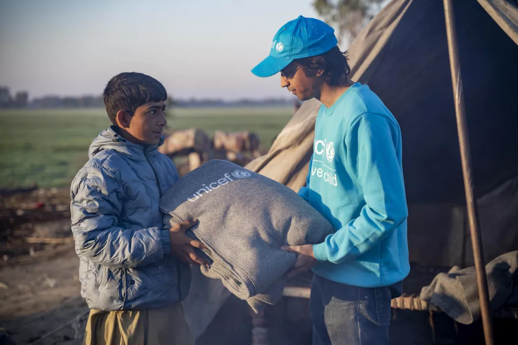 Pakistan. A UNICEF Communications Officer hands a blanket to a child in Dadu District, Sindh, Pakistan.