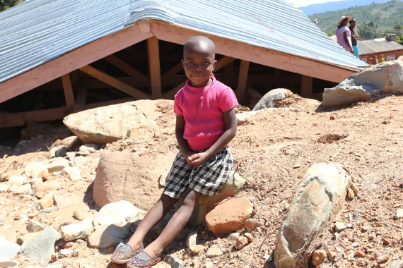Zimbabwe. A girl sits in front of the remains of her home.